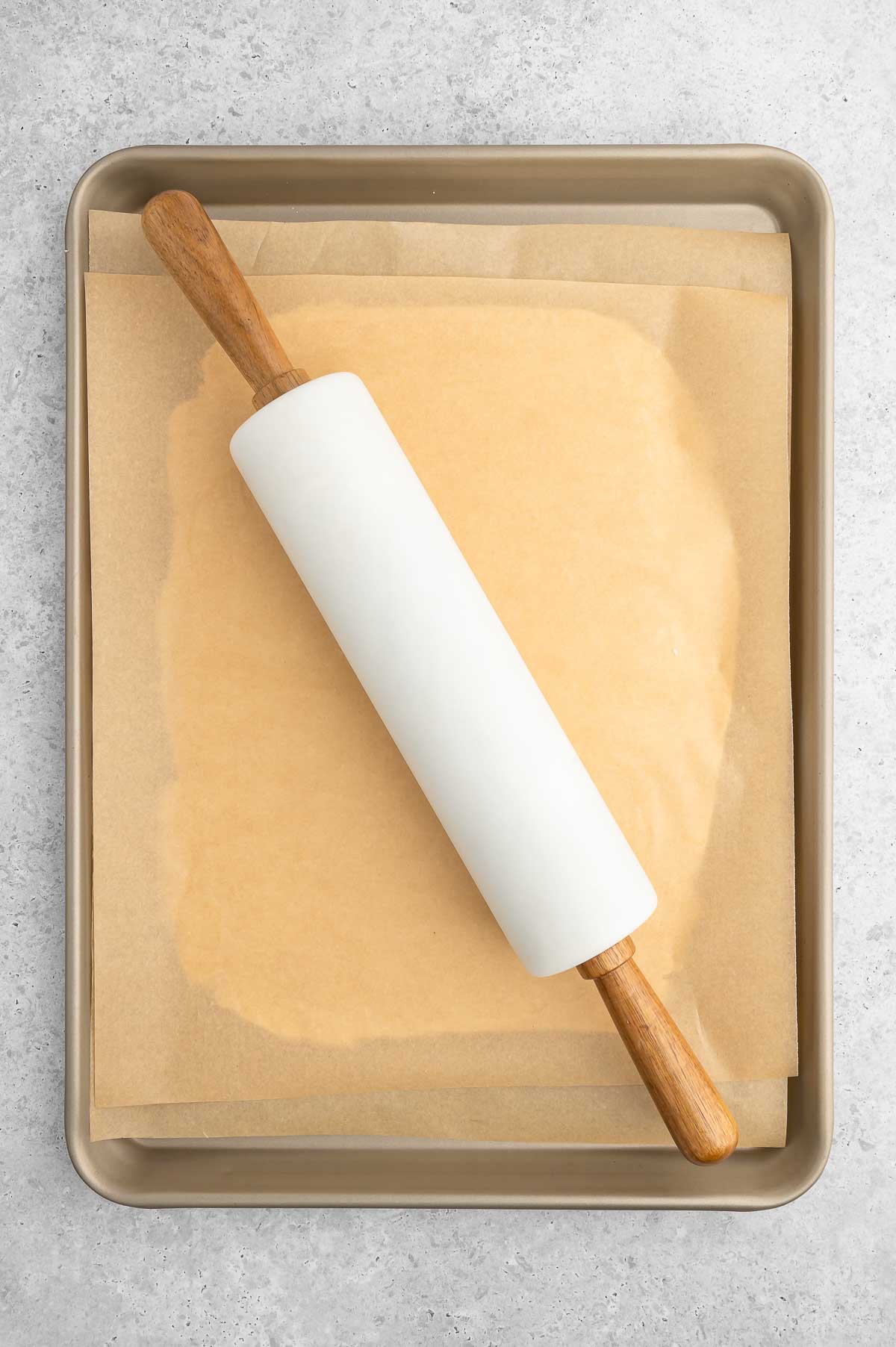 A rolling pin flattening out the pot pie crust that's between two sheets of parchment paper.