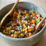 A bowl of vegan bean salad with three beans, corn, tomato, and a zesty dressing.
