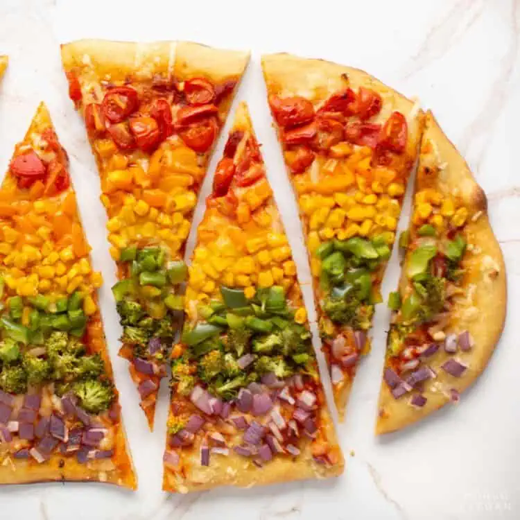 Rainbow pizza with colorful veggies sliced on a cutting board.