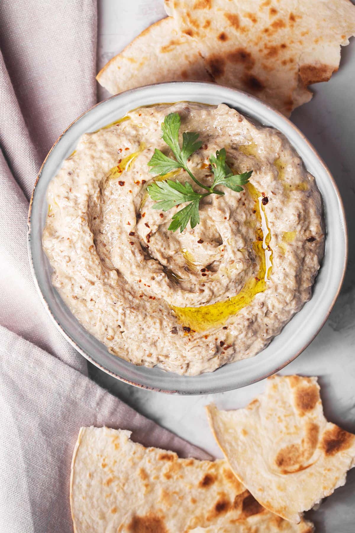 Baba ganoush dip drizzled with olive oil in a bowl next to pieces of pita bread.
