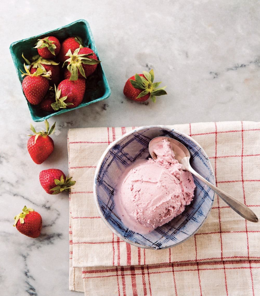 vegan strawberry ice cream in a bowl with a basket of strawberries in the top right corner for decoration