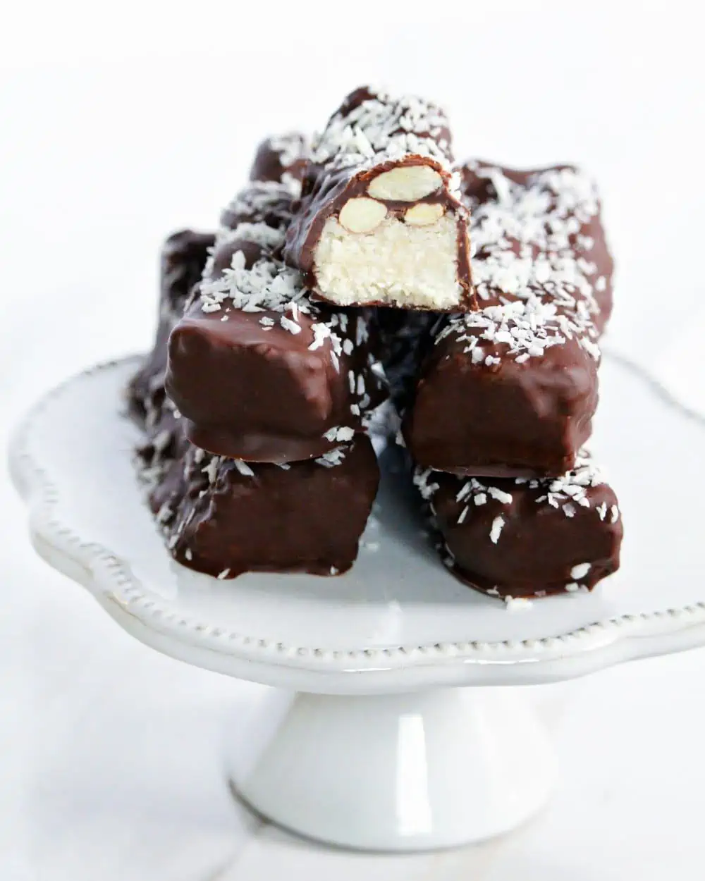 Vegan Almond Joy Bars sprinkled with coconut shreds stacked on a white cake stand.