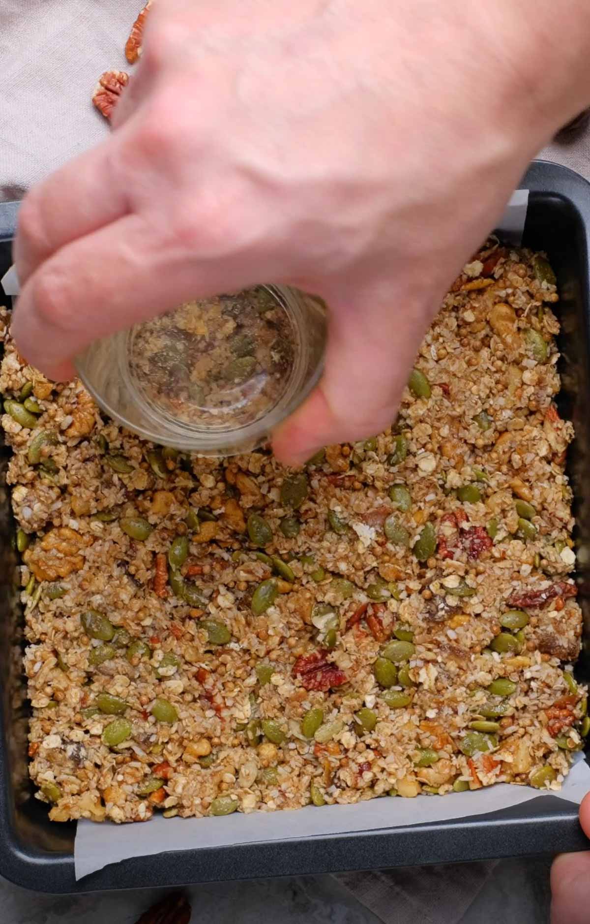 Homemade vegan granola bar mixture being pressed down with a glass.