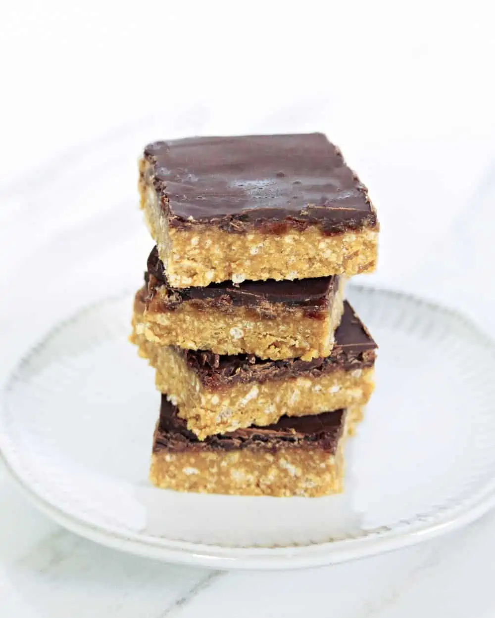 Crispy Caramel Squares stacked on a plate topped with chocolate. 