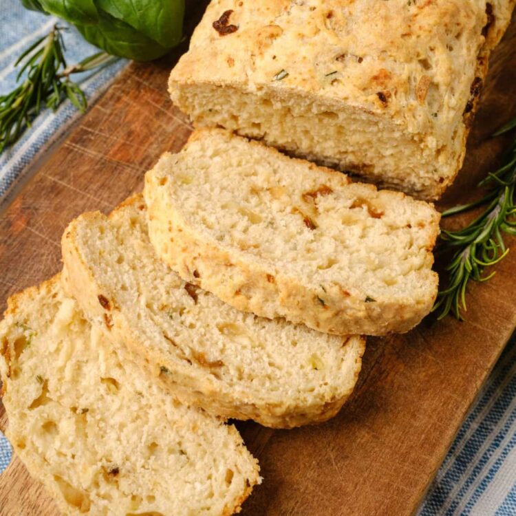 A rosemary beer bread loaf cut into slices on a cutting board.