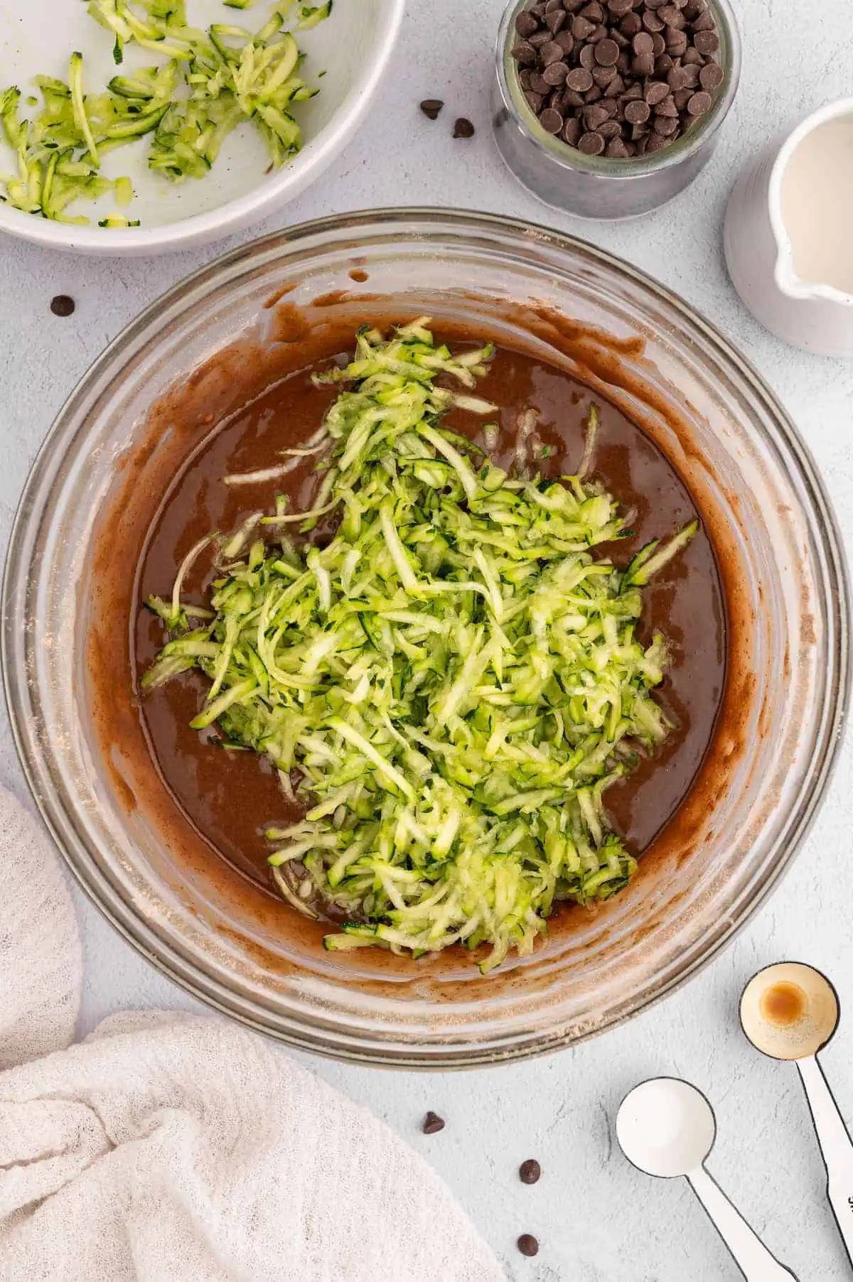 Shredded zucchini on top of vegan chocolate zucchini bread batter in a bowl.