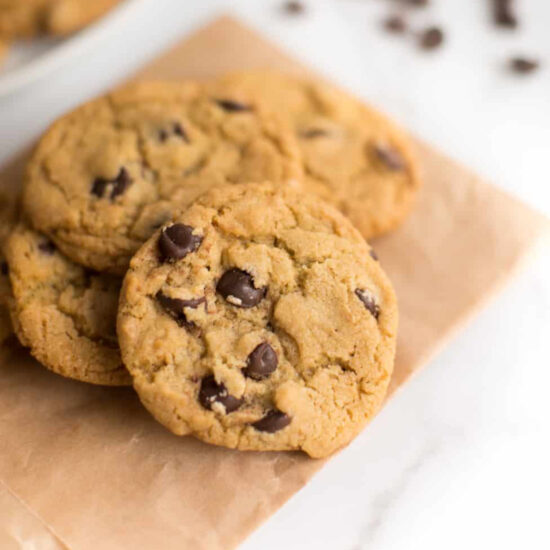 Vegan chocolate chip cookies piled on a piece of parchment paper.