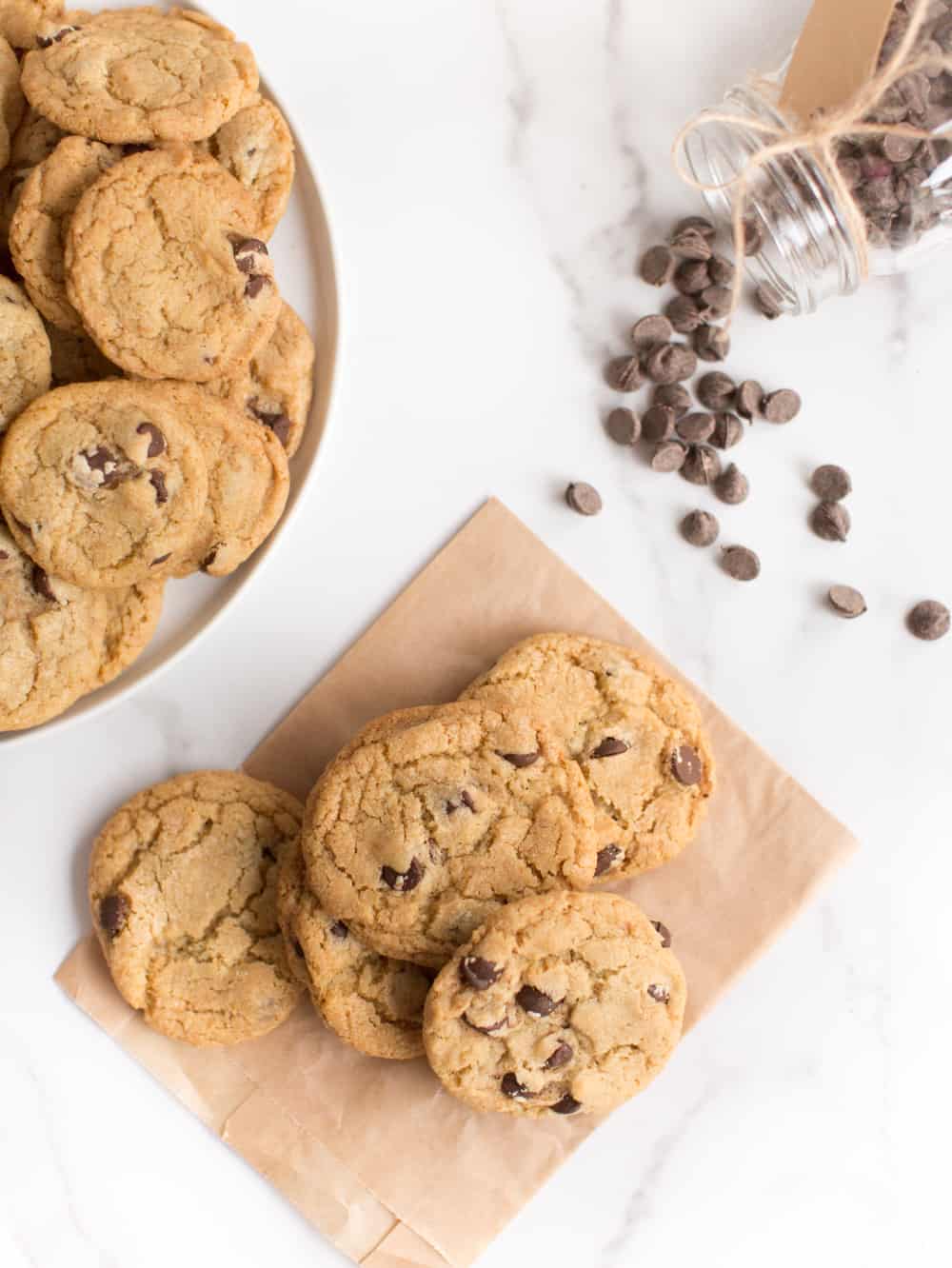 Chocolate chips spilled out of a jar next to vegan cookies.