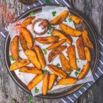 Air fried potato wedges served on a platter, sprinkled with flaky salt and fresh herbs.