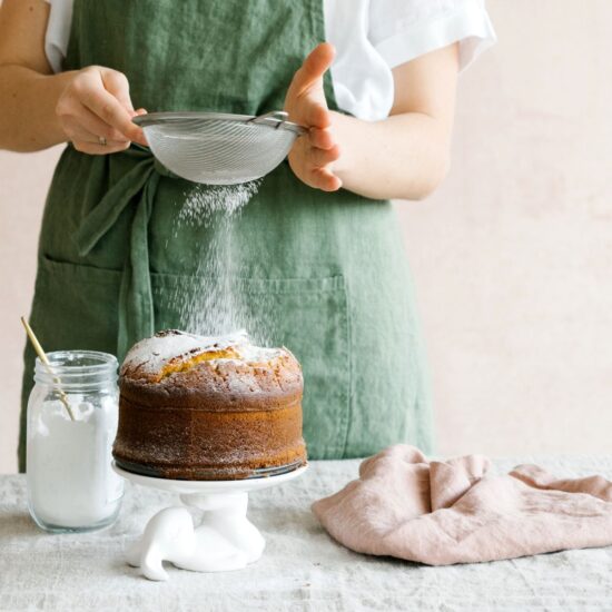 A woman sprinkling powdered sugar over a cake.