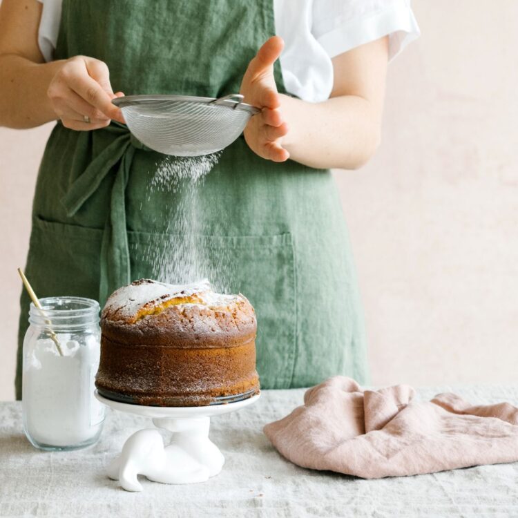 A woman sprinkling powdered sugar over a cake.
