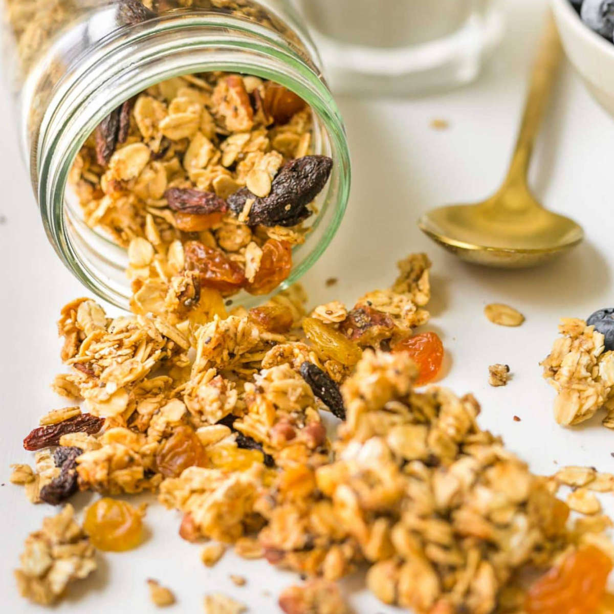 Vegan granola spilling out of a glass jar on to a countertop.
