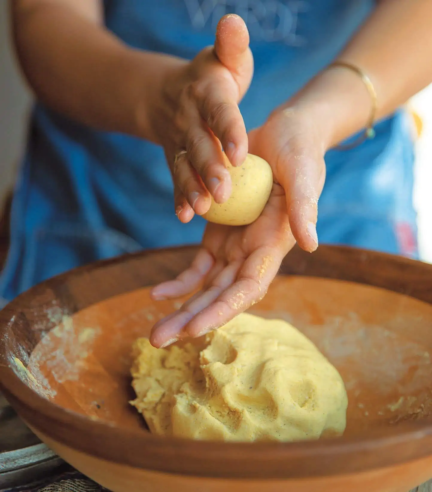 Woman holding dough in hands and rolling it to make corn tortillas.