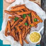 Air fryer sweet potato fries served on parchment paper with a a side of mustard dip.
