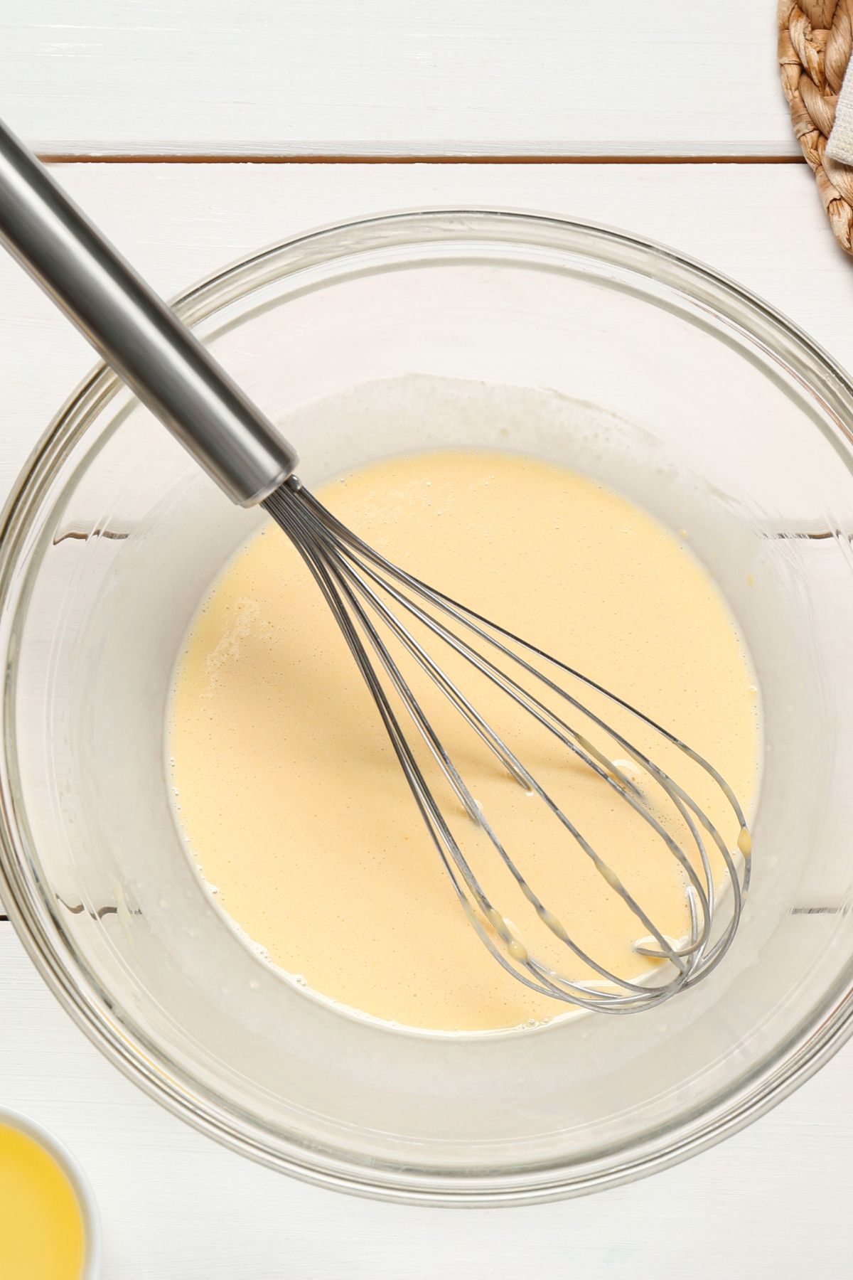 Vegan crepe batter all mixed together in a glass bowl with a whisk.