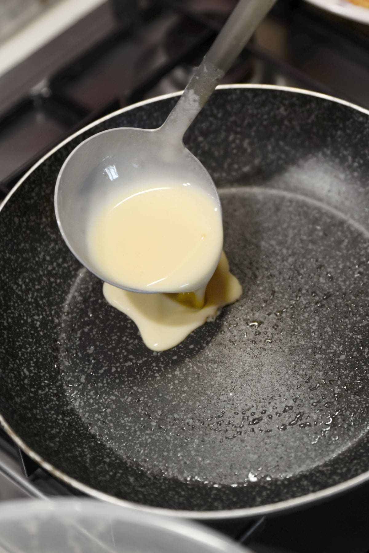 A ladle with vegan crepe batter pouring into an oiled pan.