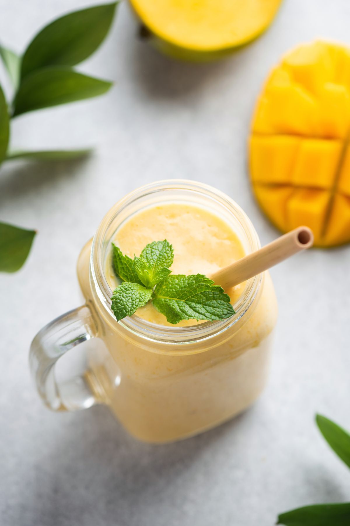 Overhead view of mango banana smoothie served in a glass jar with a straw and mint leaves.