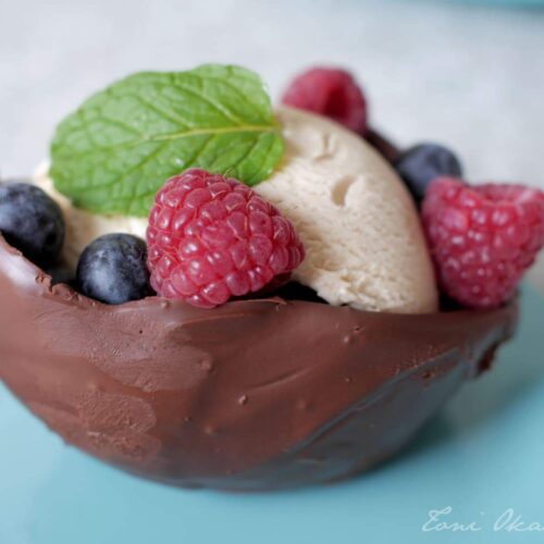 vegan chocolate bowl filled with vanilla ice cream and garnished with blueberries, raspberries, and a mint leaf