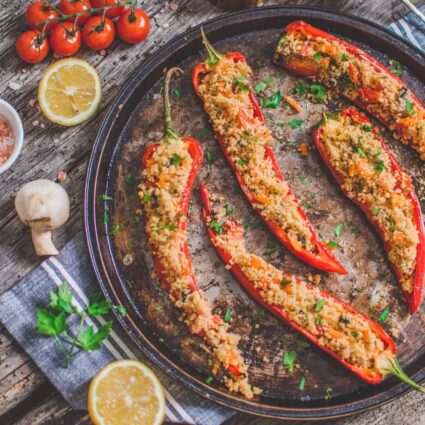 Vegan couscous stuffed peppers baked and garnished with parsley, served with lemon wedges.