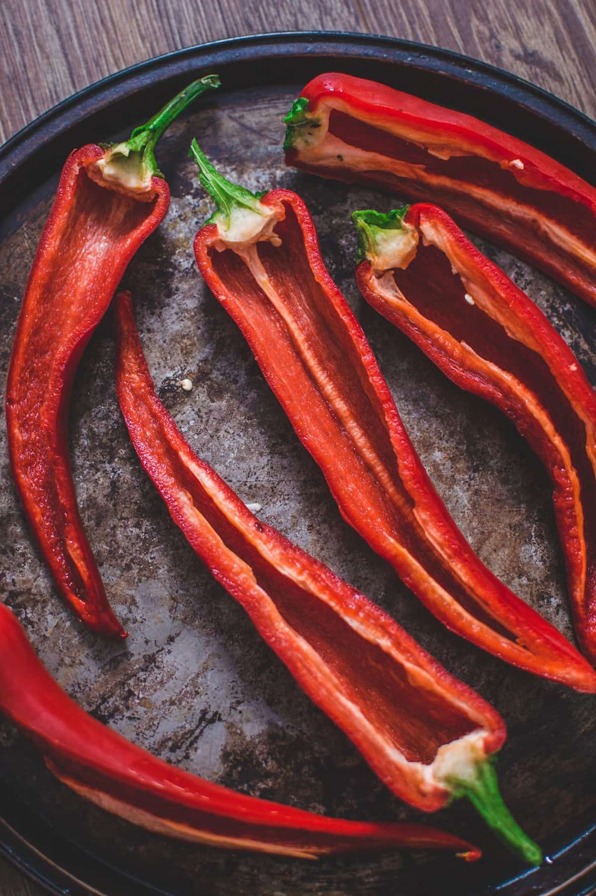 Red Romano peppers halved lengthwise on a baking sheet, ready to be filled for couscous stuffed peppers.
