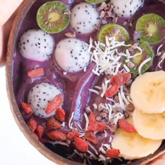 Close-up of a vibrant purple açaí bowl topped with dragonfruit, kiwi, banana, goji berries, and shredded coconut.