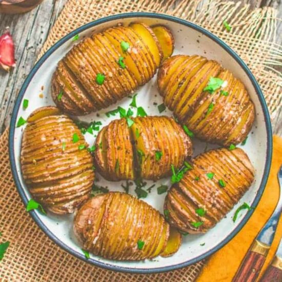 A plate of vegan Hasselback potatoes, with crispy edges and garnished with herbs.