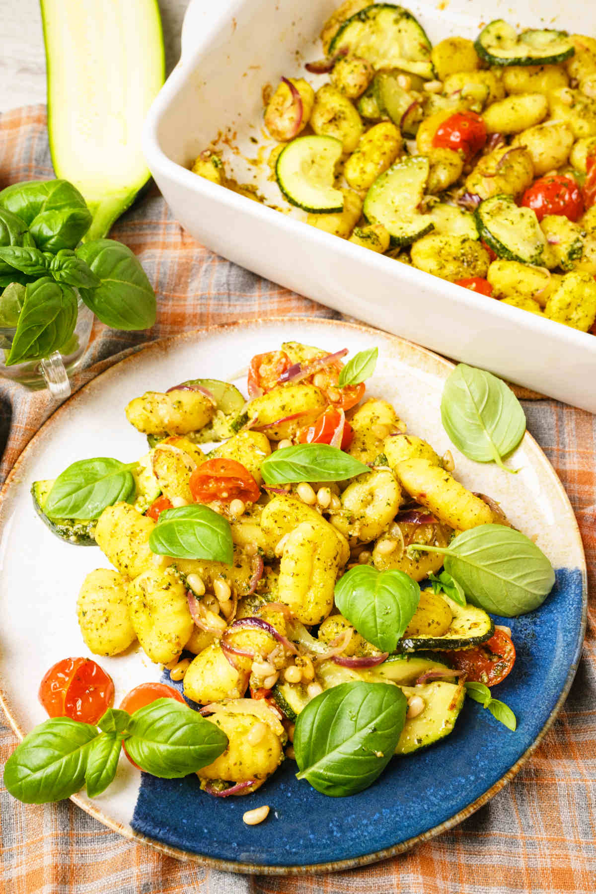 Pesto gnocchi on a plate next to a casserole dish with it.