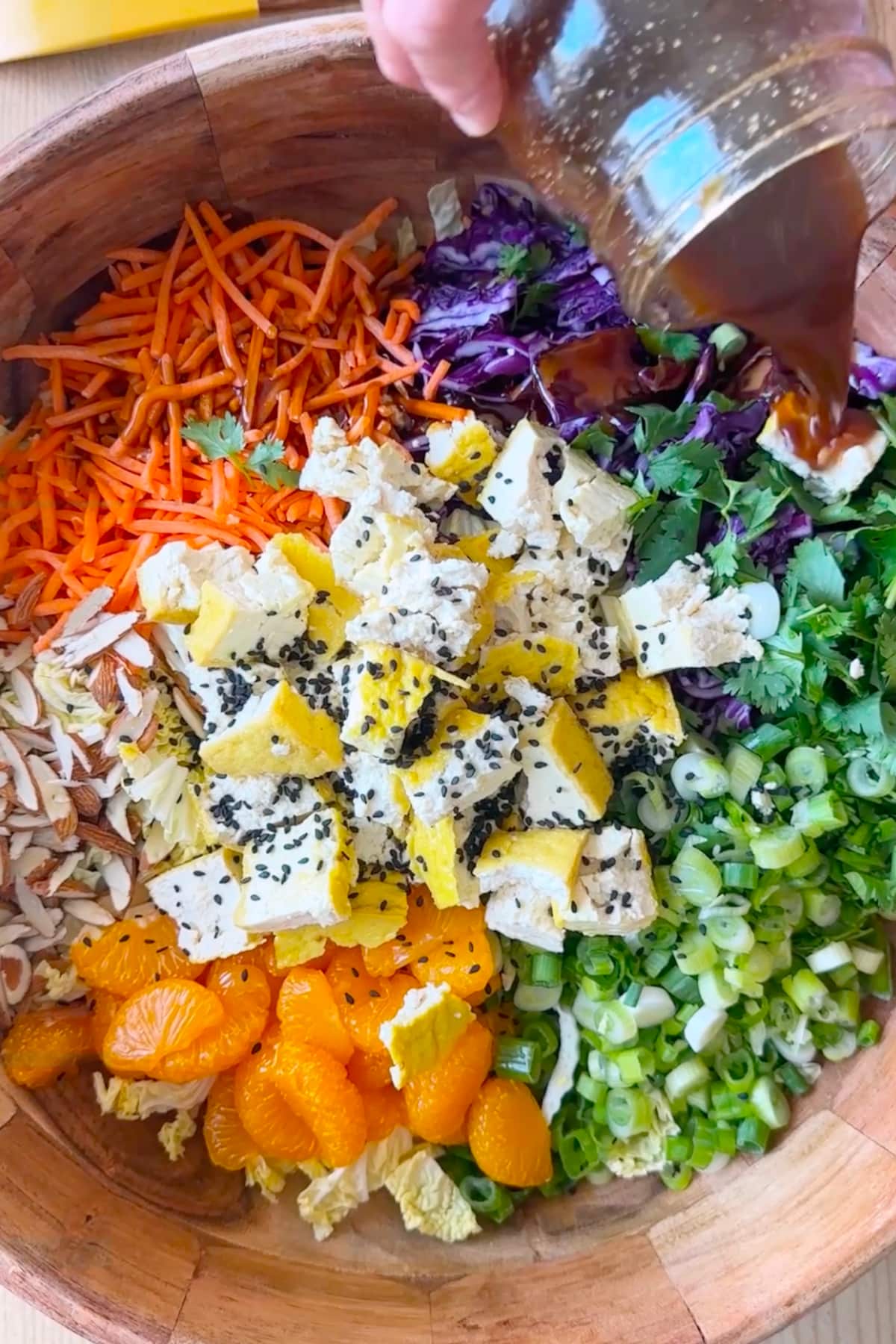 The dressing being poured over the vegan asian salad in a large wooden bowl.