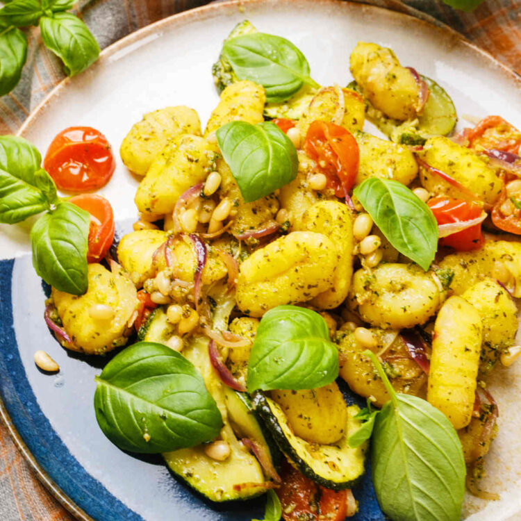 Pesto gnocchi served on a plate with fresh basil leaves.