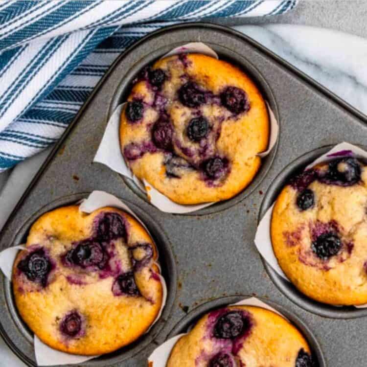Vegan blueberry muffins in a baking pan next to a blue striped dish towel.