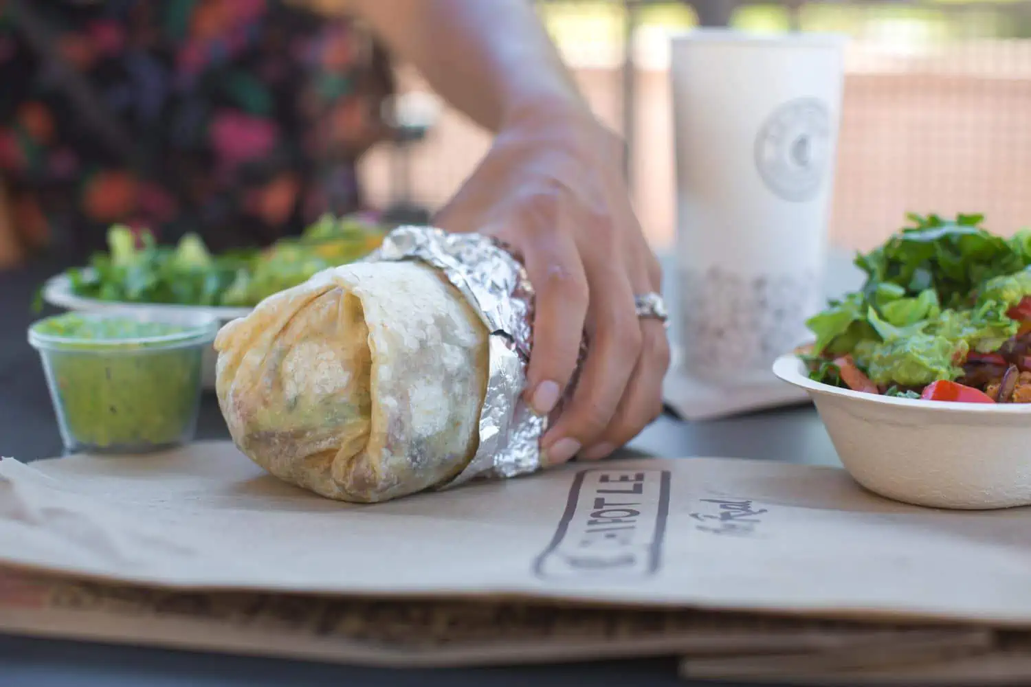 Woman Eating a Vegan Chipotle Burrito at the Outdoor Tables of the Restaurant