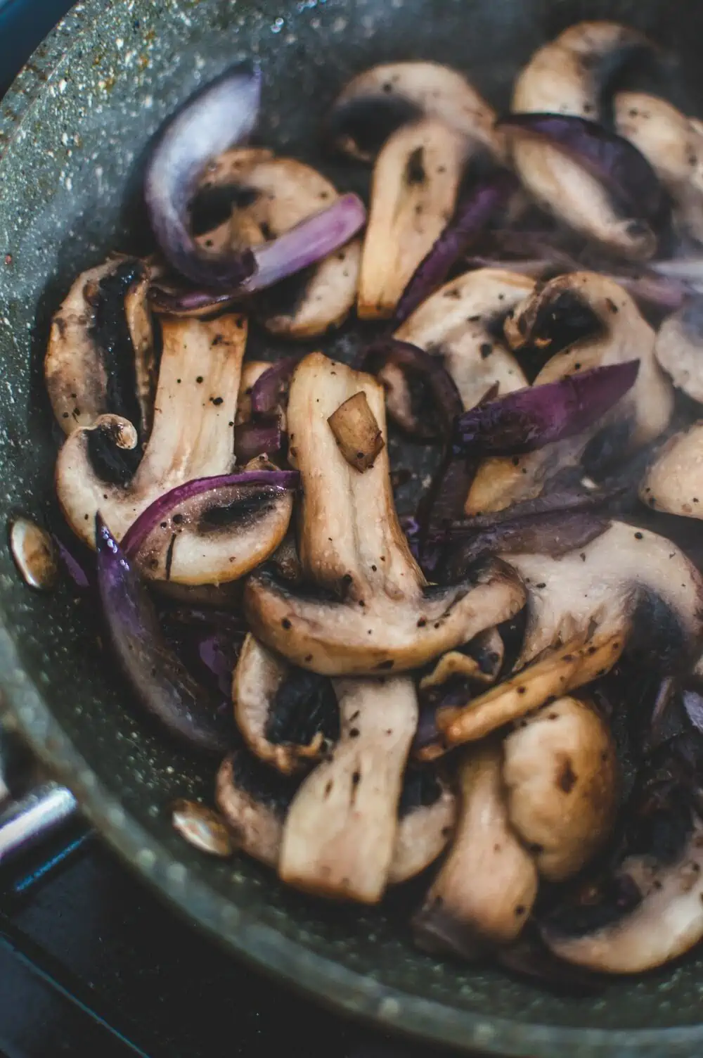Mushrooms and red onion sauteing in a pan.