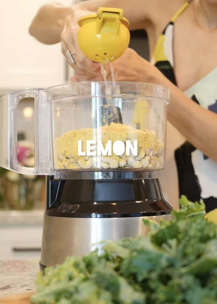 squeezing lemon into a food processor with cashews making kale chip paste