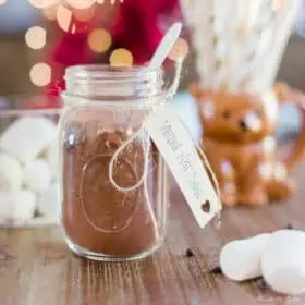 Homemade Vegan Hot Cocoa Mix in a mason jar on a wooden table with Christmas lights in the background.