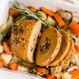 Tofurky roast sliced, in a baking dish on top of roasted vegetables.