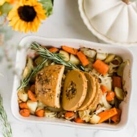 Tofurky roast sliced, in a baking dish on top of roasted vegetables.