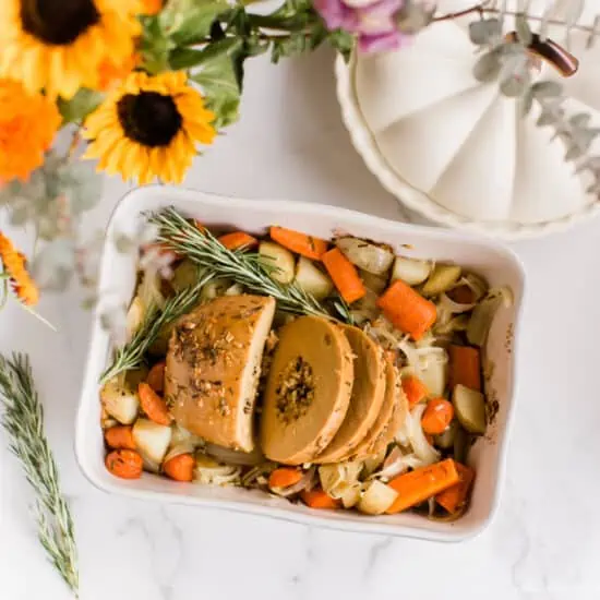 Tofurky roast sliced, in a baking dish on top of roasted vegetables.