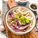 Bowl of Purple Udon Noodle Soup Served over a Wooden Board Close Up