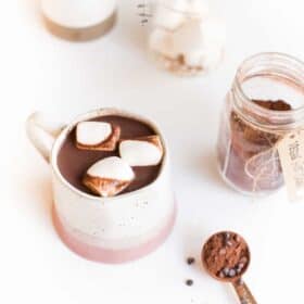Vegan hot chocolate in a mug topped with marshmallows next to a jar of vegan hot cocoa mix.