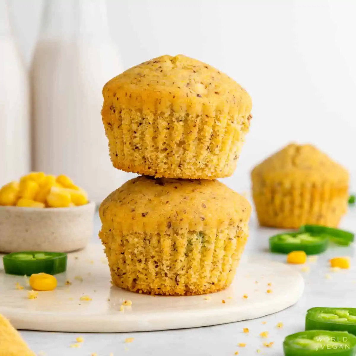 Two vegan cornbread muffins with jalapeno stacked on a white plate.