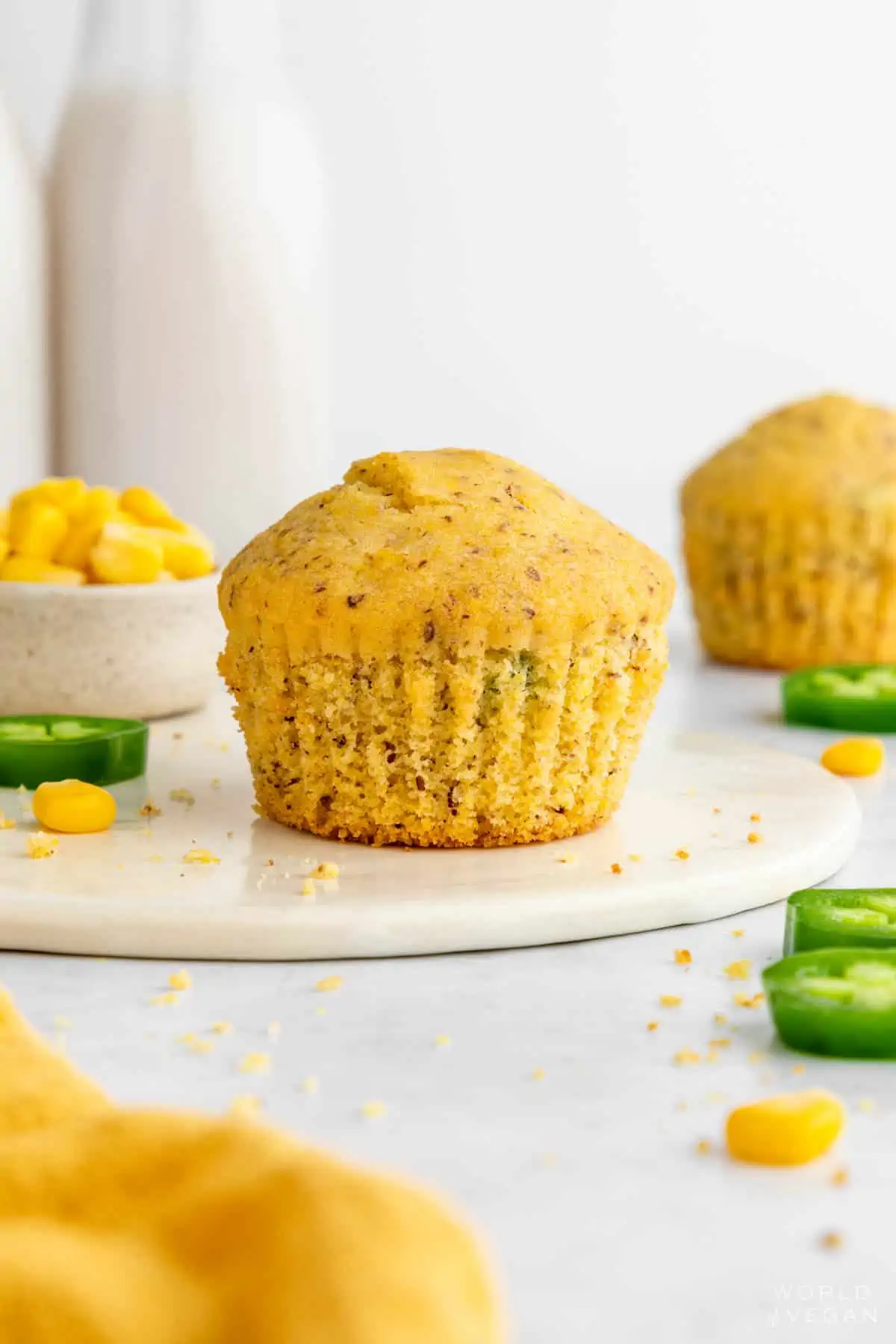 Vegan cornbread muffin up close with jalapenos and corn kernels scattered around it.