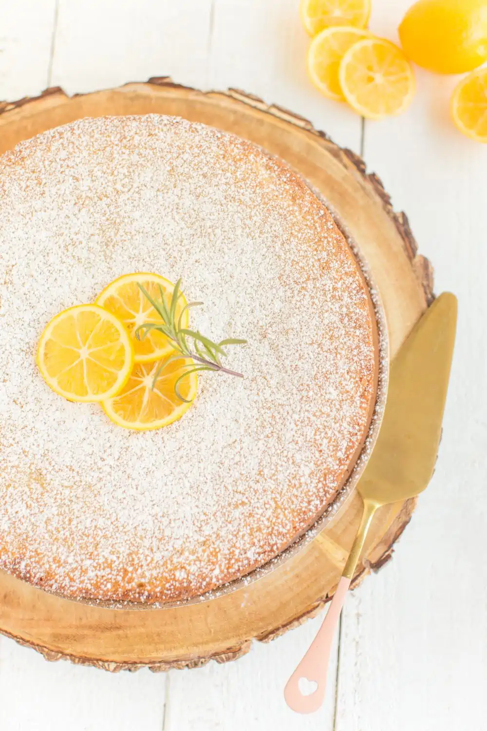 Vegan Lemon Olive Oil Cake topped with sliced lemons and rosemary and served on a rustic wooden cake stand