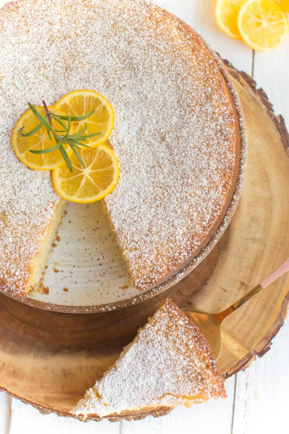 Sliced Lemon Olive Oil Cake garnished with powdered sugar and three lemon slices on top