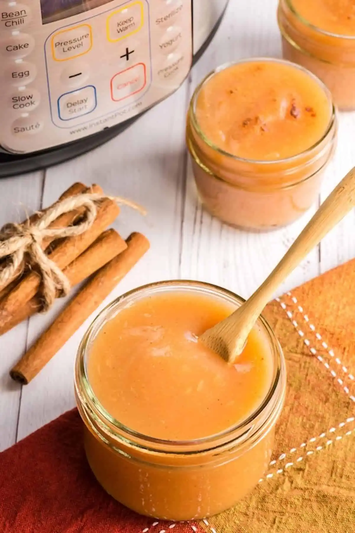 Two small jars of instant pot applesauce next to cinnamon sticks.