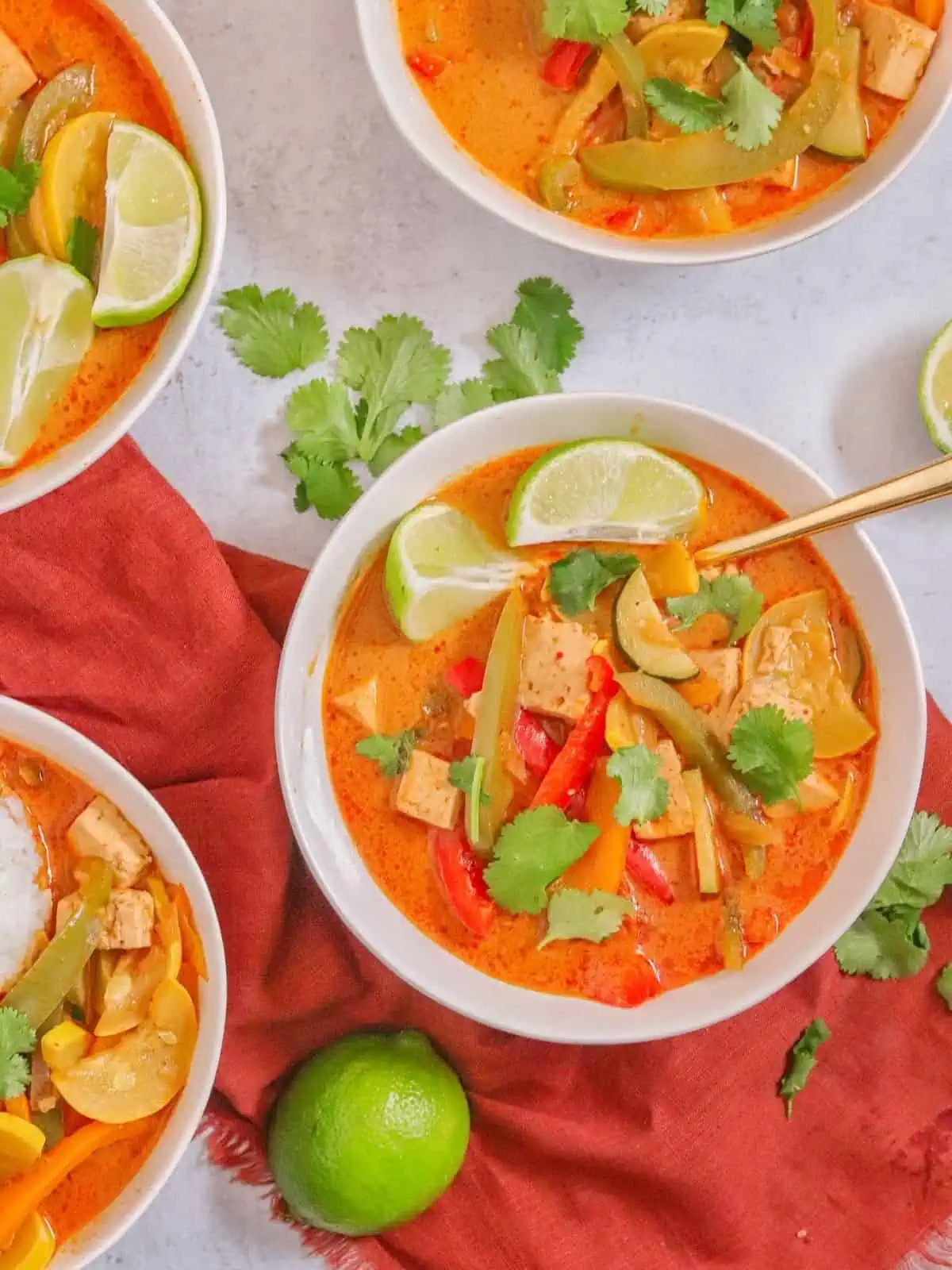 Four bowls of vegan Thai panang curry topped with lime wedges and fresh cilantro leaves.