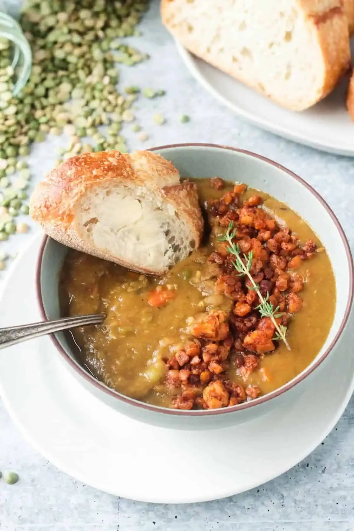 A bowl of vegan split pea soup served with tempeh crumbles and a slice of crusty bread.