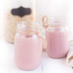 Two Mason Jars filled with Strawberries and Cream Smoothie and a container of Oats