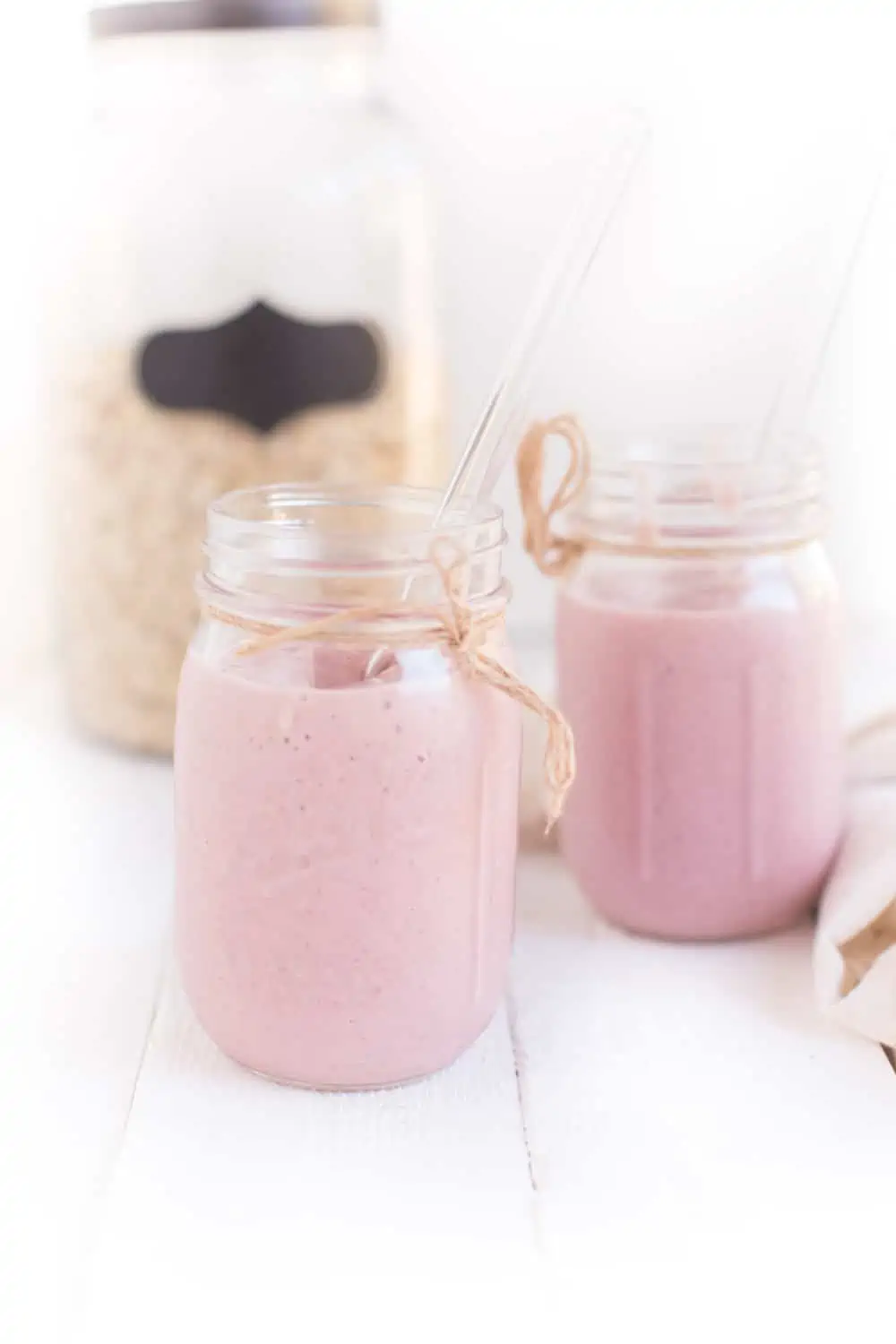 Two Mason Jars filled with Strawberries and Cream Smoothie and a container of Oats