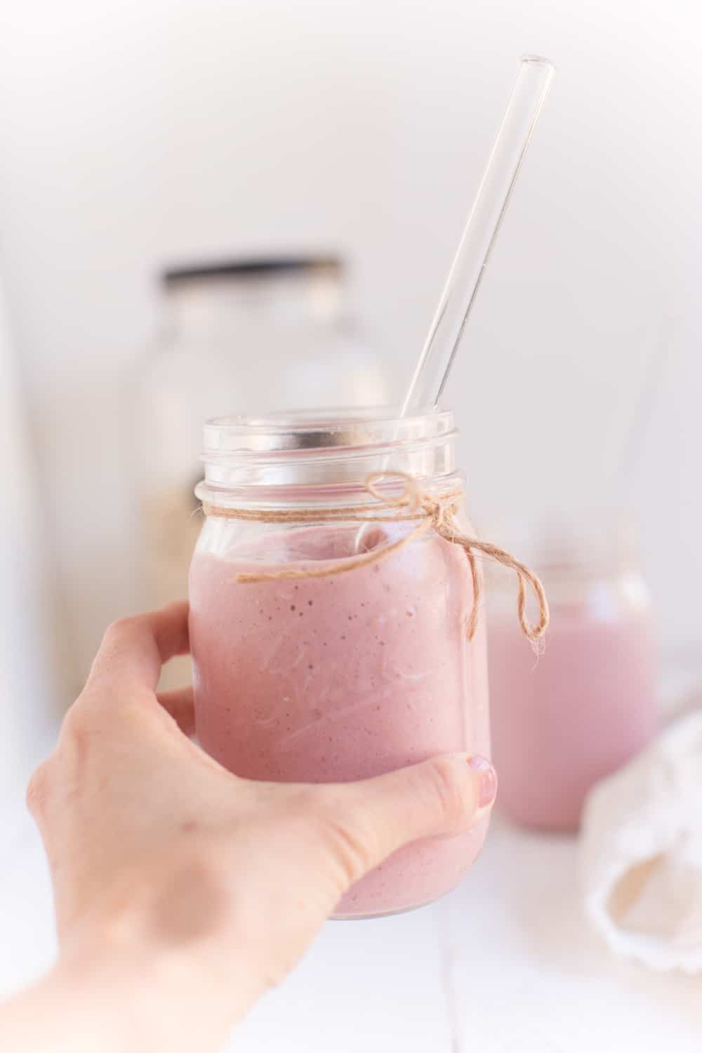 Hand holding a mason jar filled with a strawberry and cream smoothie