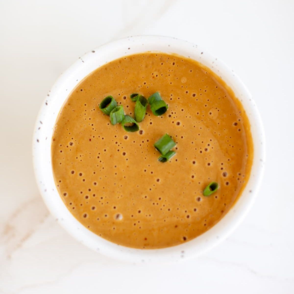 A bowl of peanut dipping sauce with chopped scallions.